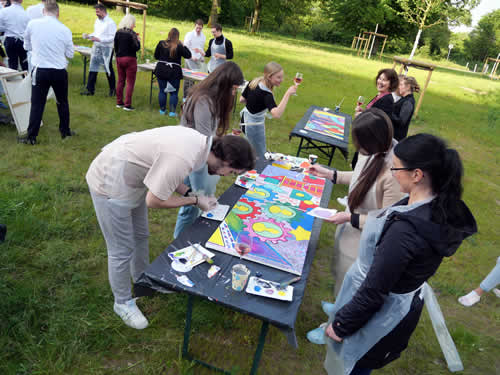 kreative Mitarbeiter malen engagiert ihr großes gemeinschaftskunstwerk auf dem Sommerfest